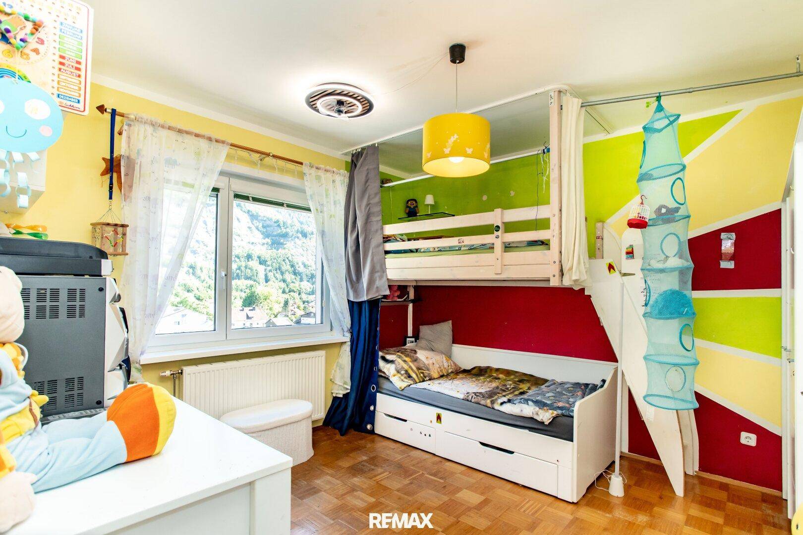 Farbenfrohes Kinderzimmer mit Hochbett, Spielbereich und hellem Fenster mit Ausblick.