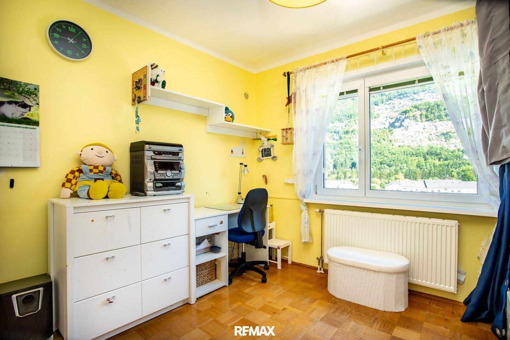 Helles Kinderzimmer mit Schreibtisch, Stauraum und großem Fenster mit Blick ins Grüne.