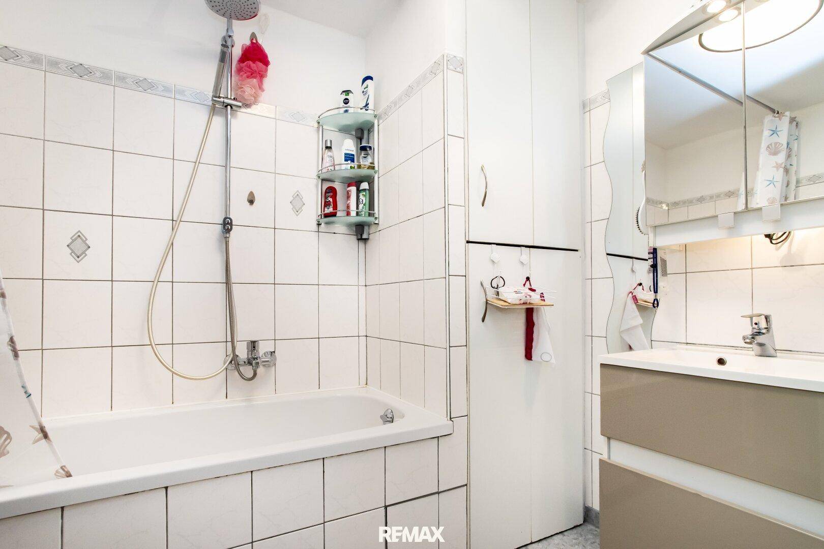 Funktionales Badezimmer mit Badewanne, Duschfunktion, Waschbecken und Spiegelschrank.