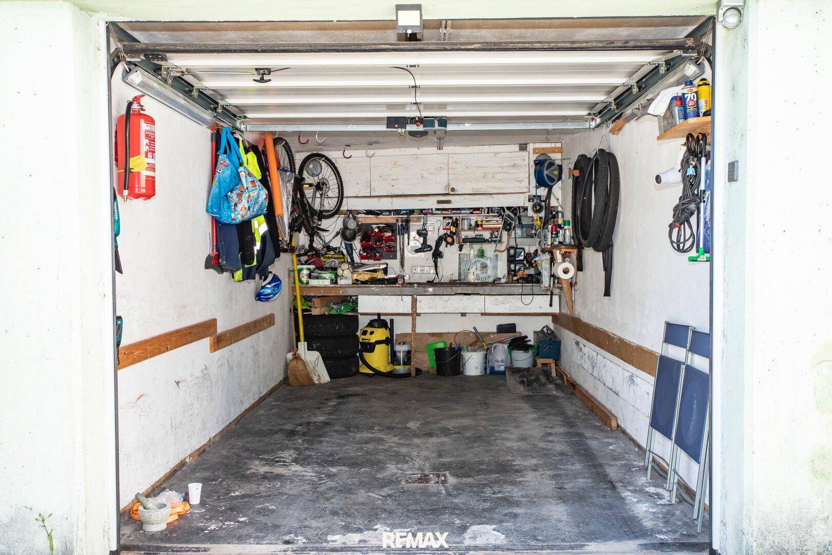 Geräumige Garage mit Werkbank, Regalen und ausreichend Platz für Fahrzeuge und Lagerung.