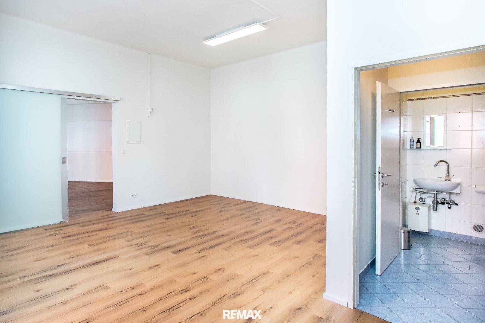 Heller Raum mit Holzboden und offenem Zugang zu einem Badezimmer mit blauen Fliesen.