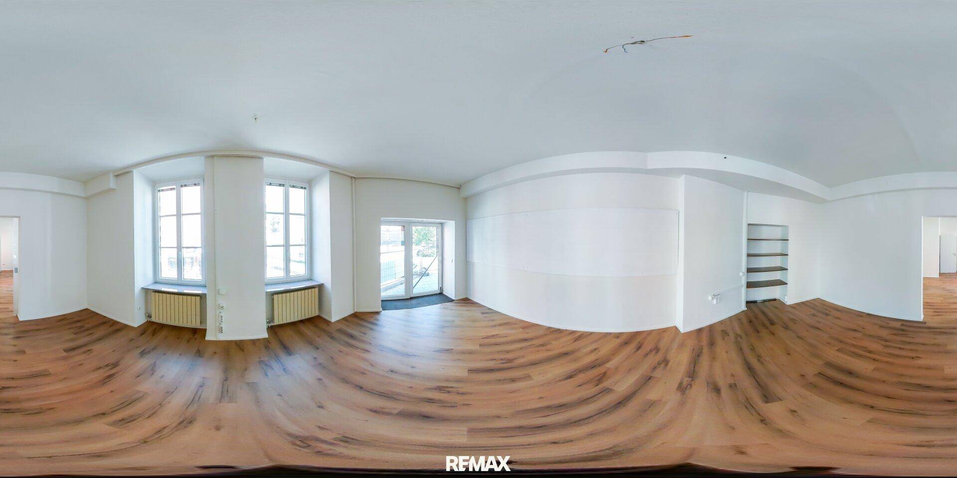 Panoramaansicht eines hellen, leeren Raumes mit Holzboden, Fenstern und Balkonzugang.