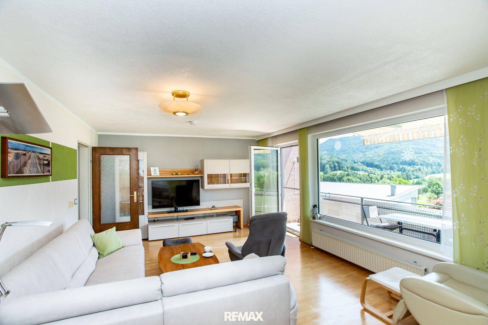 Helles Wohnzimmer mit großem Fenster, Holzboden und Panoramablick auf die umliegende Natur.