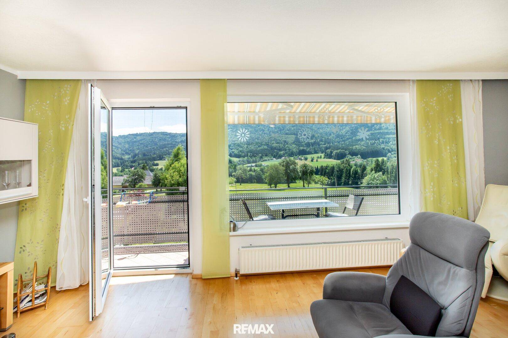 Wohnzimmer mit Zugang zum Balkon und weitem Blick über die grüne Hügellandschaft.