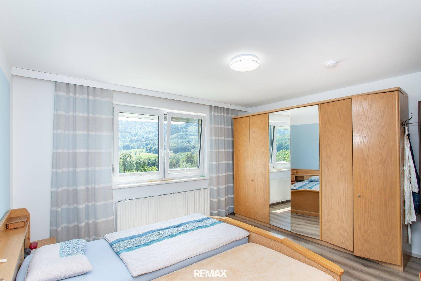 Schlafzimmer mit großem Holzschrank, Doppelbett und Fenster mit Blick ins Grüne.