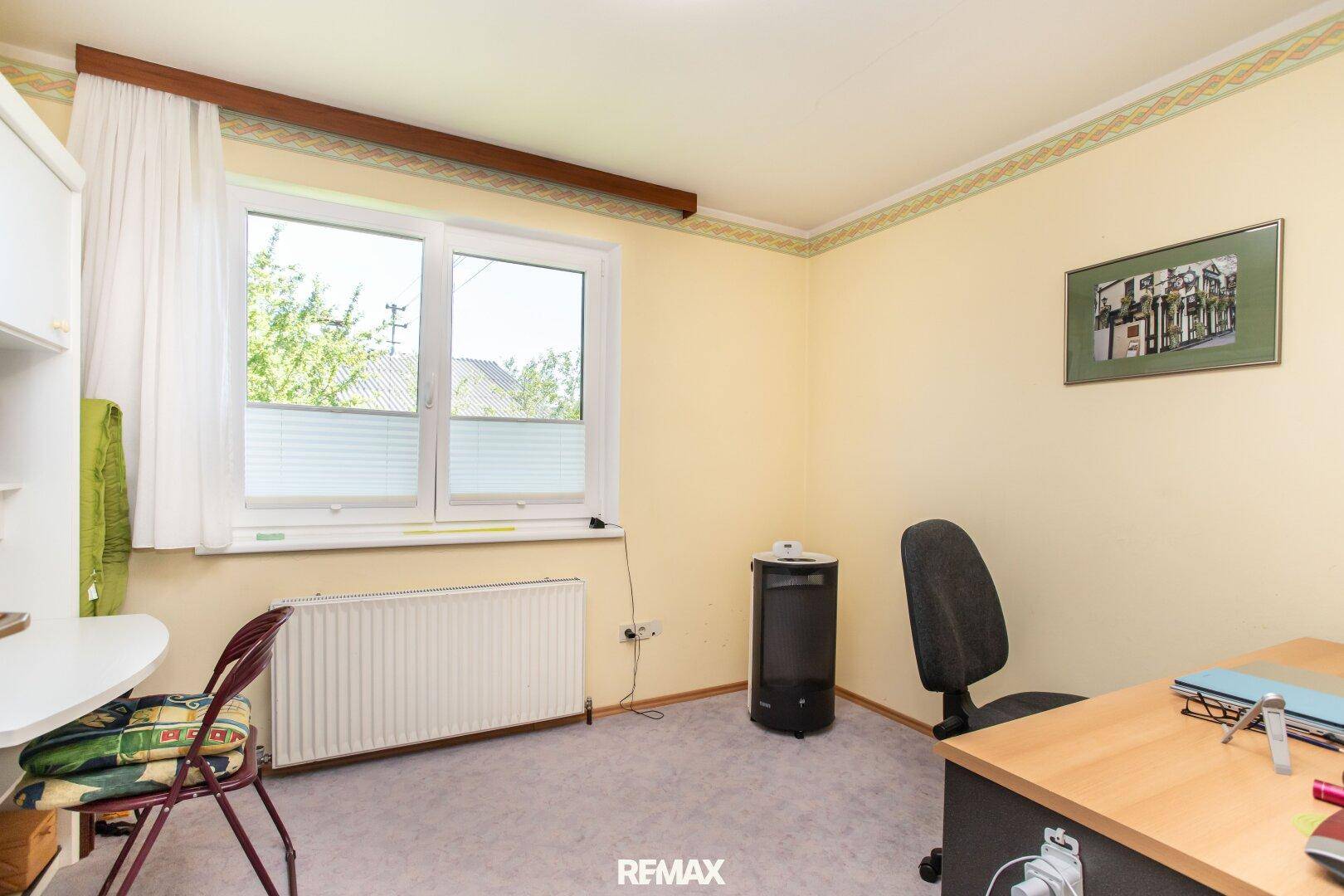 Helles Arbeitszimmer mit Schreibtisch, Bürostuhl und Fenster mit Blick nach draußen.
