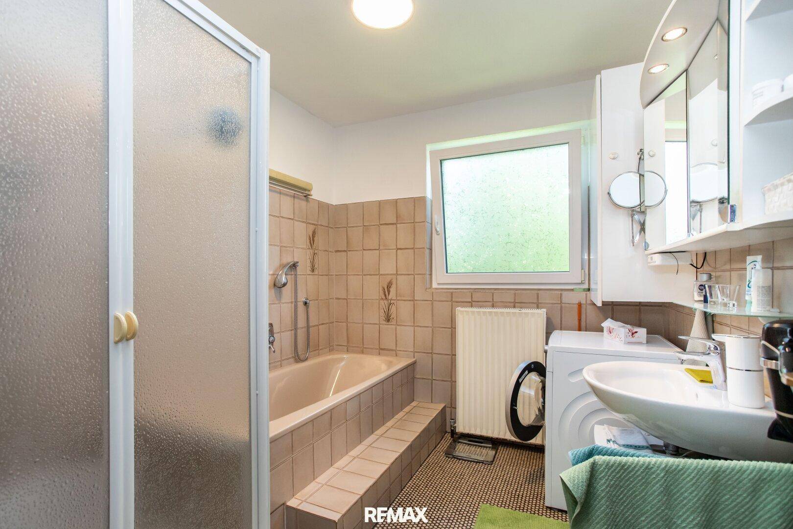 Badezimmer mit Badewanne, Duschkabine, Waschbecken und Fenster für Tageslicht.
