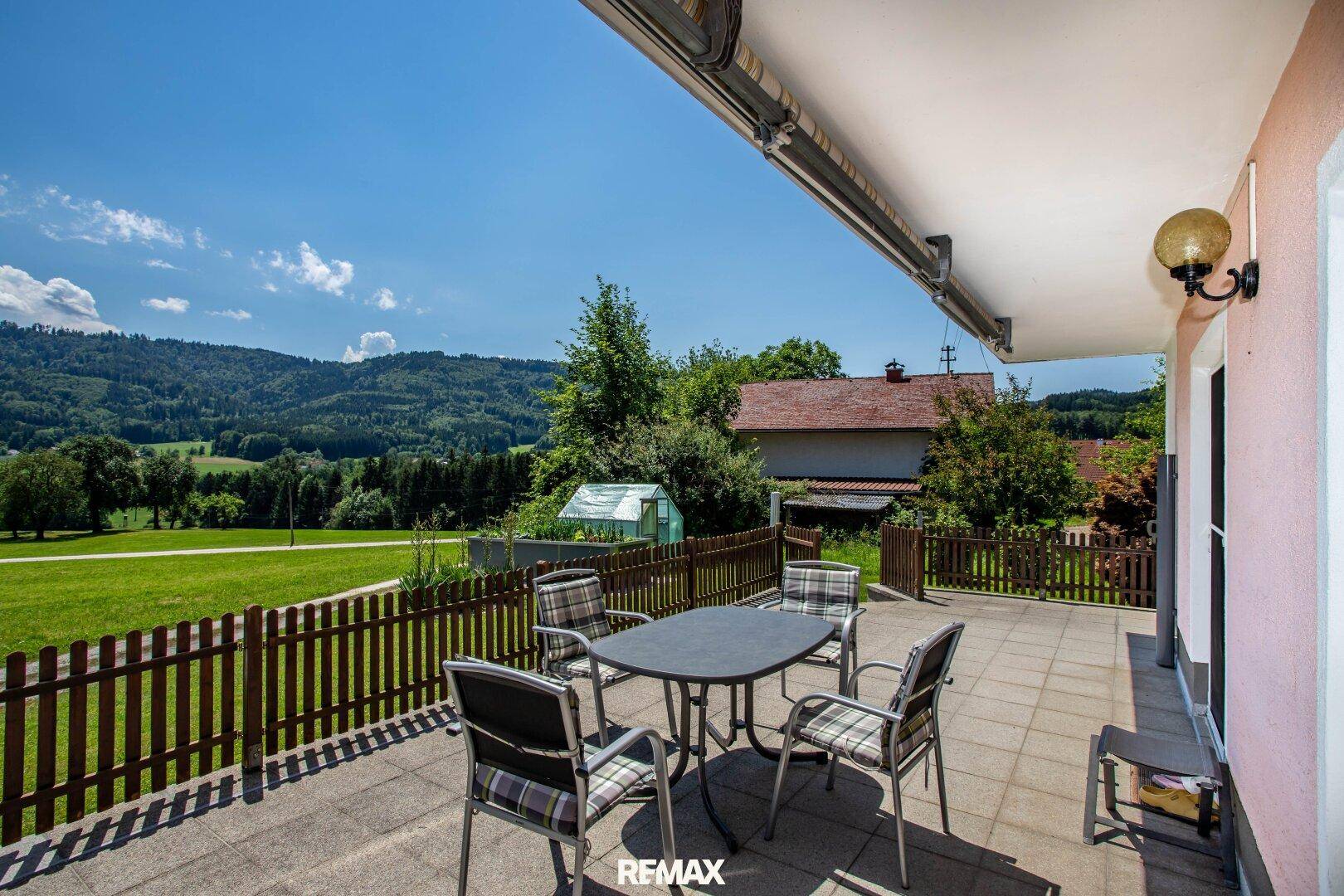 Große geflieste Terrasse mit Gartenmöbeln und Blick auf die grüne Hügellandschaft.