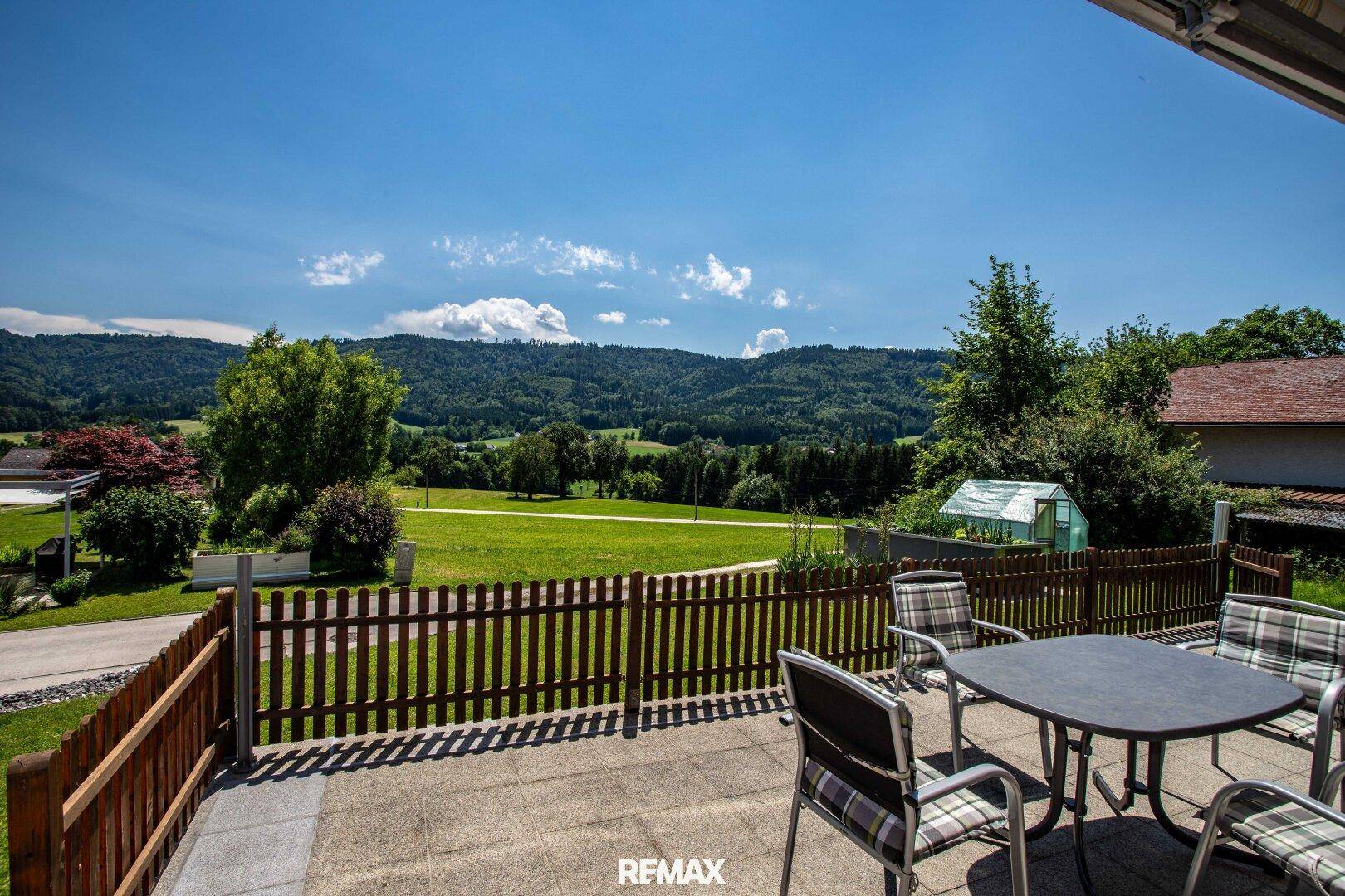 Sonniger Terrassenbereich mit Sitzgelegenheiten und weitem Blick über die grüne Landschaft.