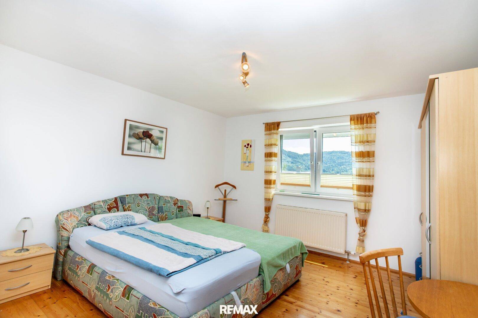Schlafzimmer mit Doppelbett, Holzmöbeln und Fenster mit Blick auf die grüne Landschaft.
