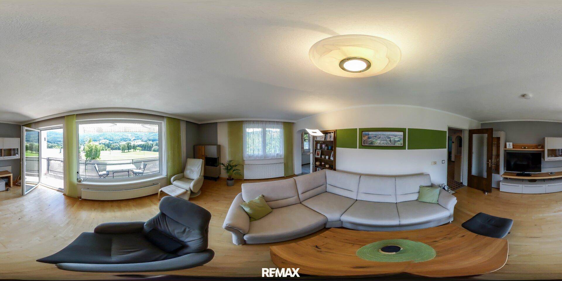 Helles Wohnzimmer mit großem Sofa, Holzboden und Zugang zu einem Balkon mit Weitblick.