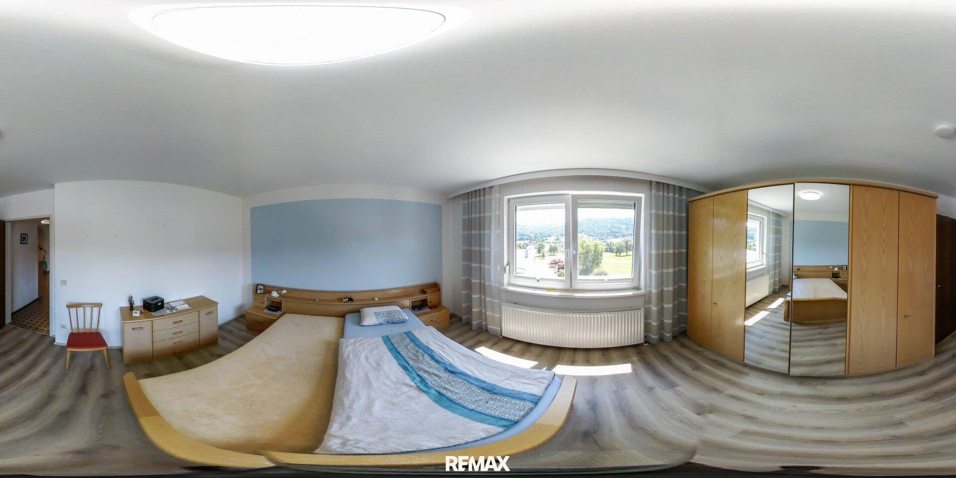 Schlafzimmer mit Doppelbett, Holzmöbeln und Fenster mit Blick ins Grüne.