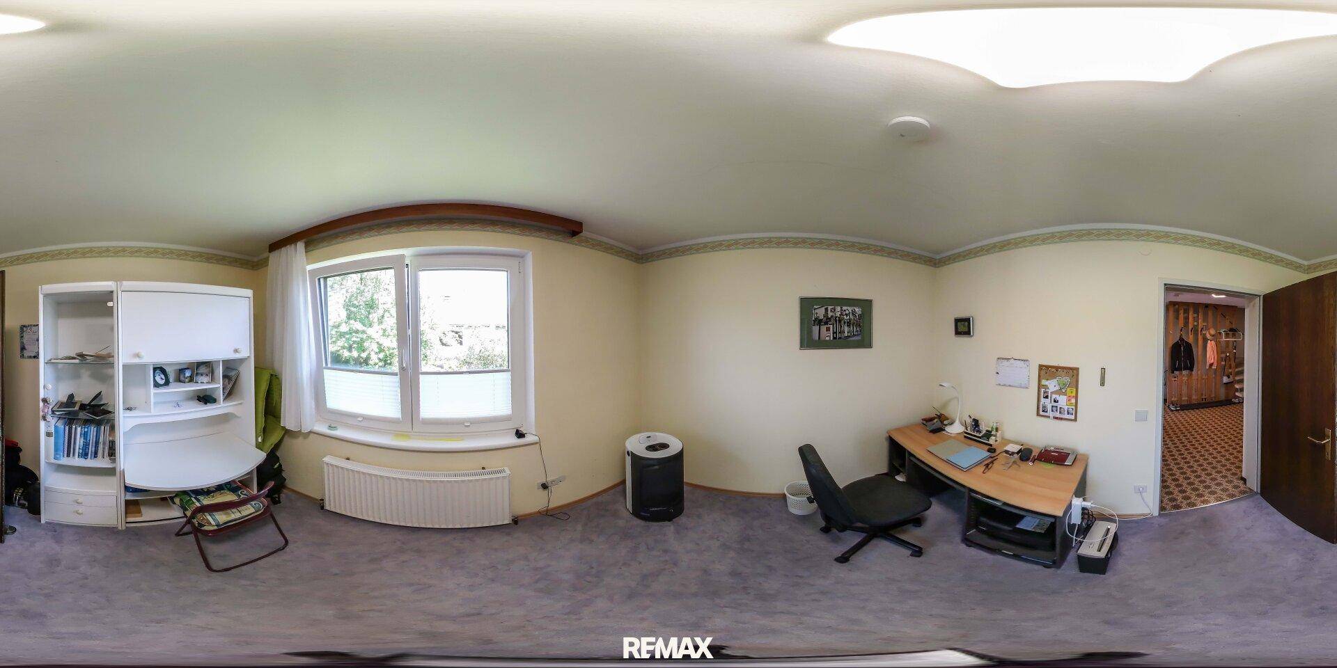 Arbeitszimmer mit Schreibtisch, Regal und Fenster mit Blick ins Grüne.