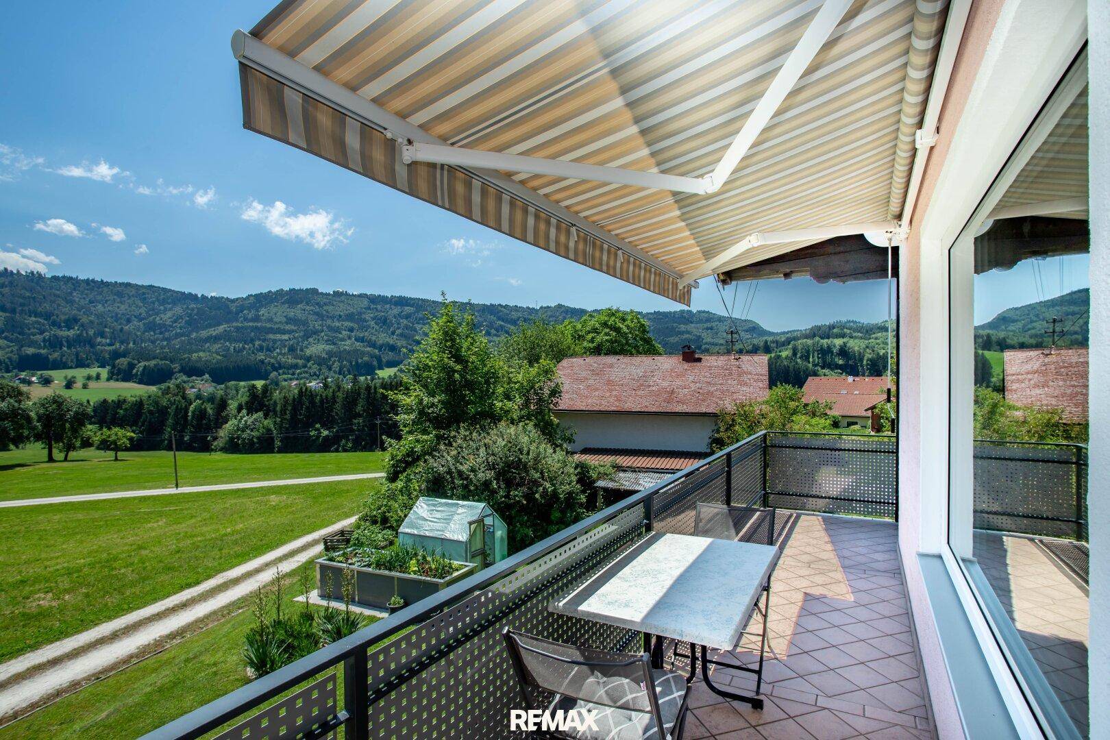 Sonniger Balkon mit Markise, Sitzgelegenheiten und weitem Blick über die grüne Landschaft.