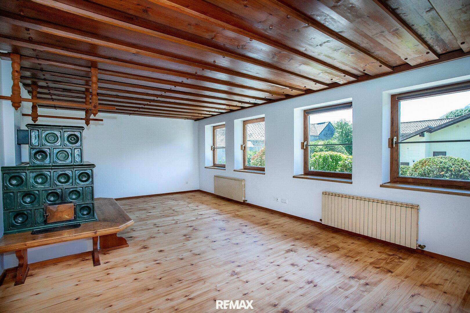 Geräumiger Raum mit Holzboden, Holzdecke und einem traditionellen Kachelofen, ideal für ein Wohnzimmer.