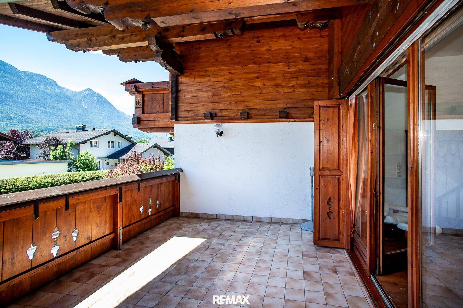 Sonniger Balkon mit Fliesenboden und traditionellem Holzgeländer, bietet einen schönen Bergblick.
