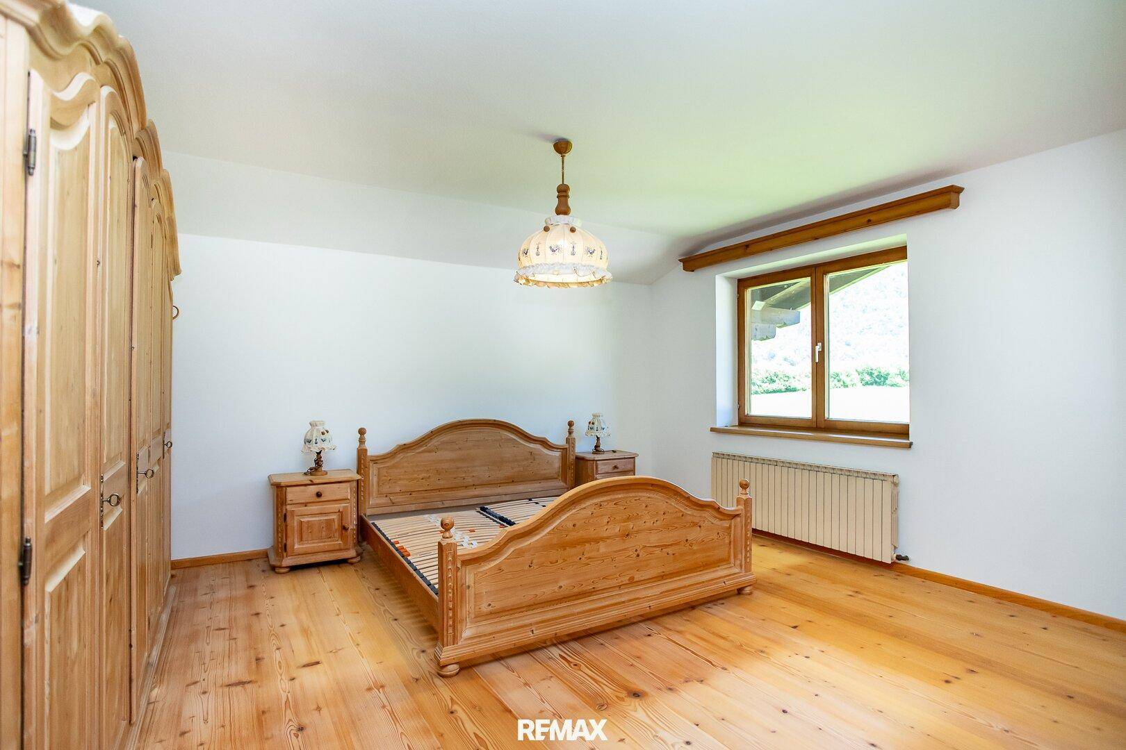Rustikales Schlafzimmer mit Holzboden, Holzmöbeln und einem Fenster mit Blick ins Grüne.