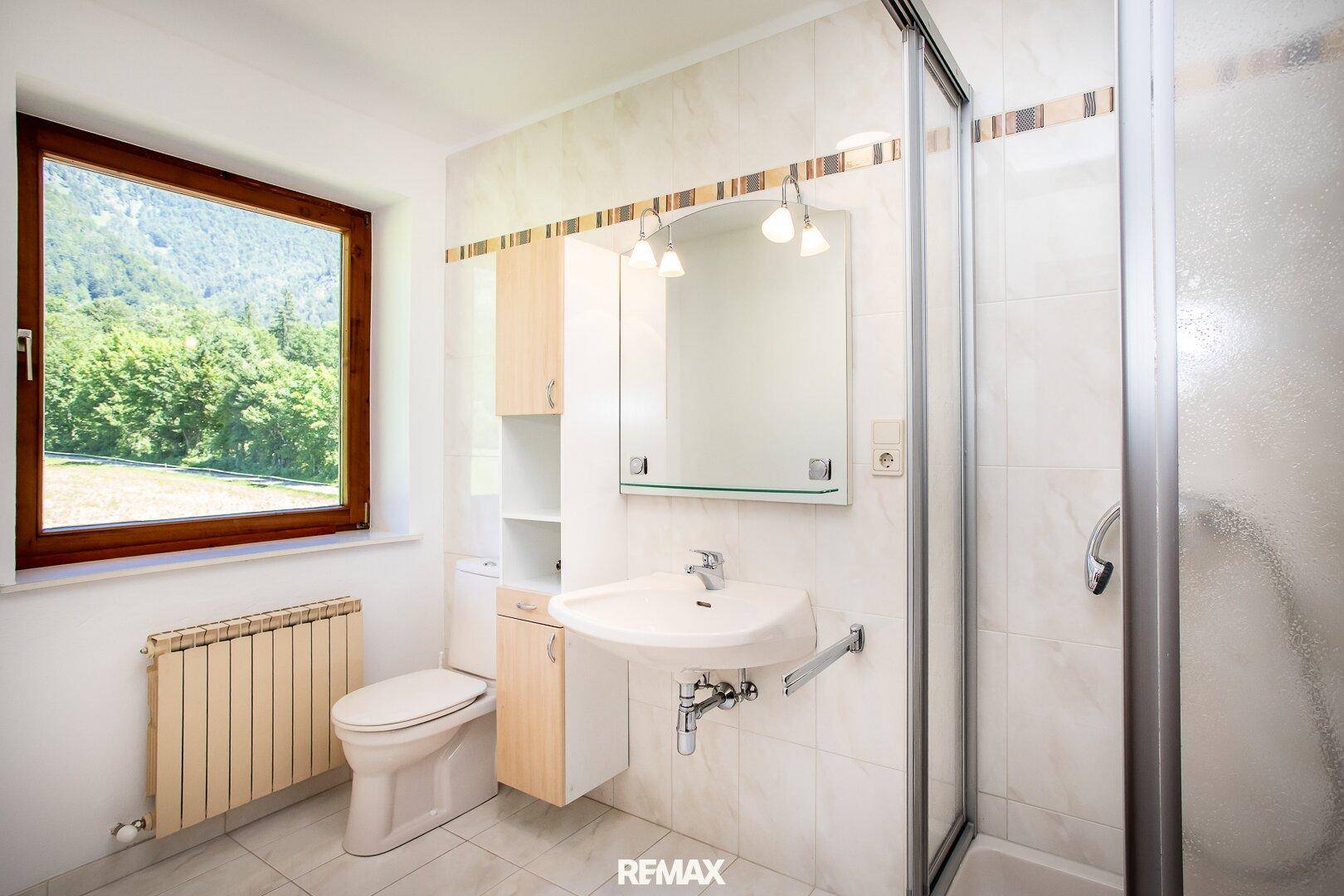 Modernisiertes Badezimmer mit Dusche, WC, Waschbecken und Fenster mit Bergblick.