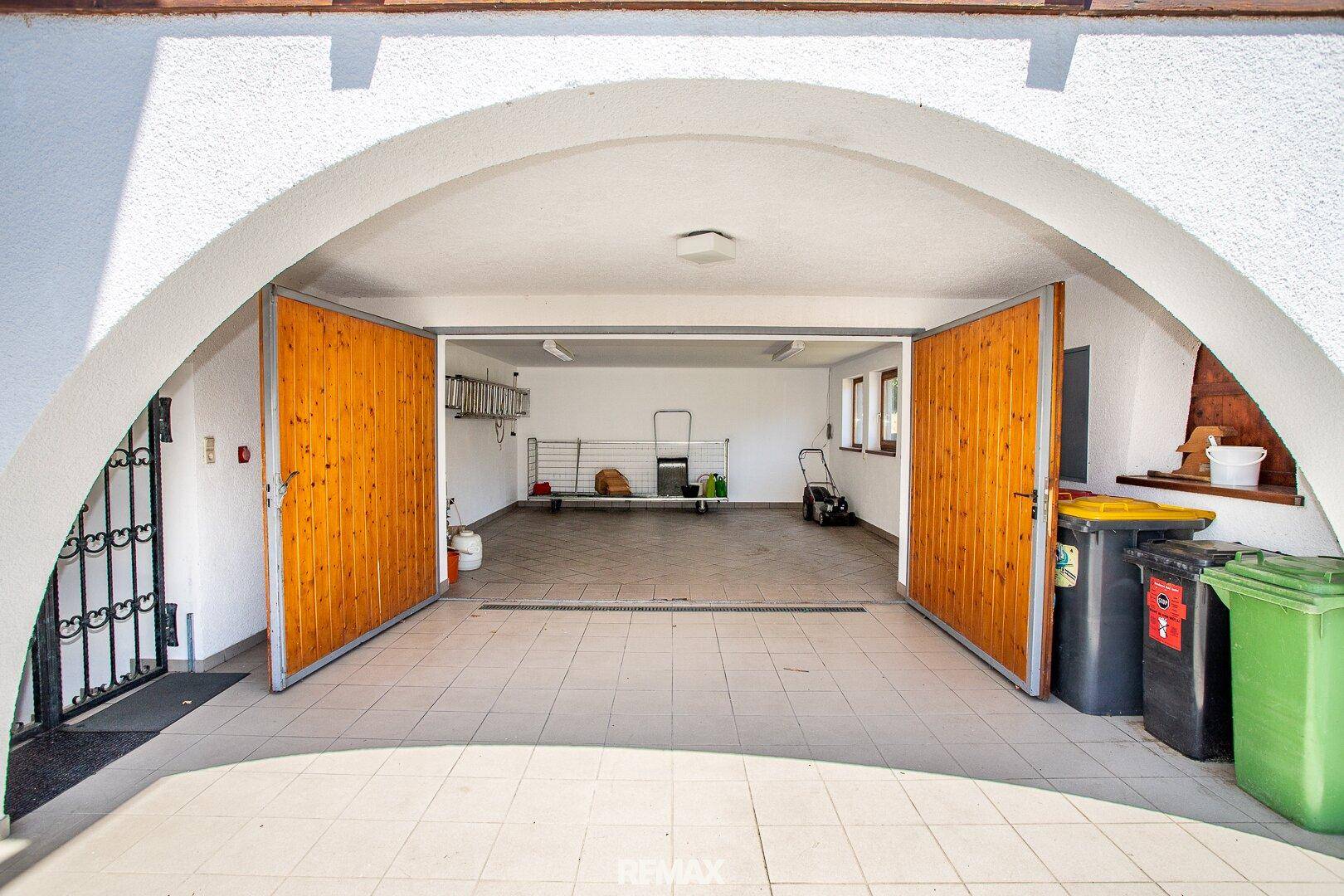 Geräumige Garage mit zwei Holztoren und Fliesenboden, bietet Platz für Fahrzeuge und Lagerung.
