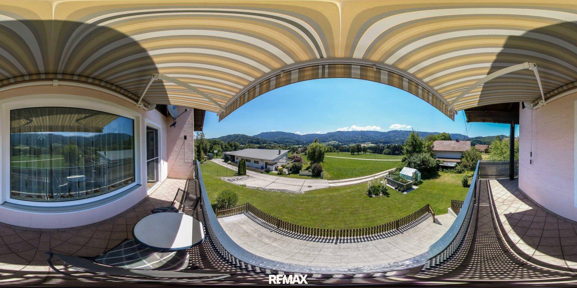 Geräumige Terrasse mit Markise, Sitzgelegenheiten und weitem Blick über die grüne Landschaft.