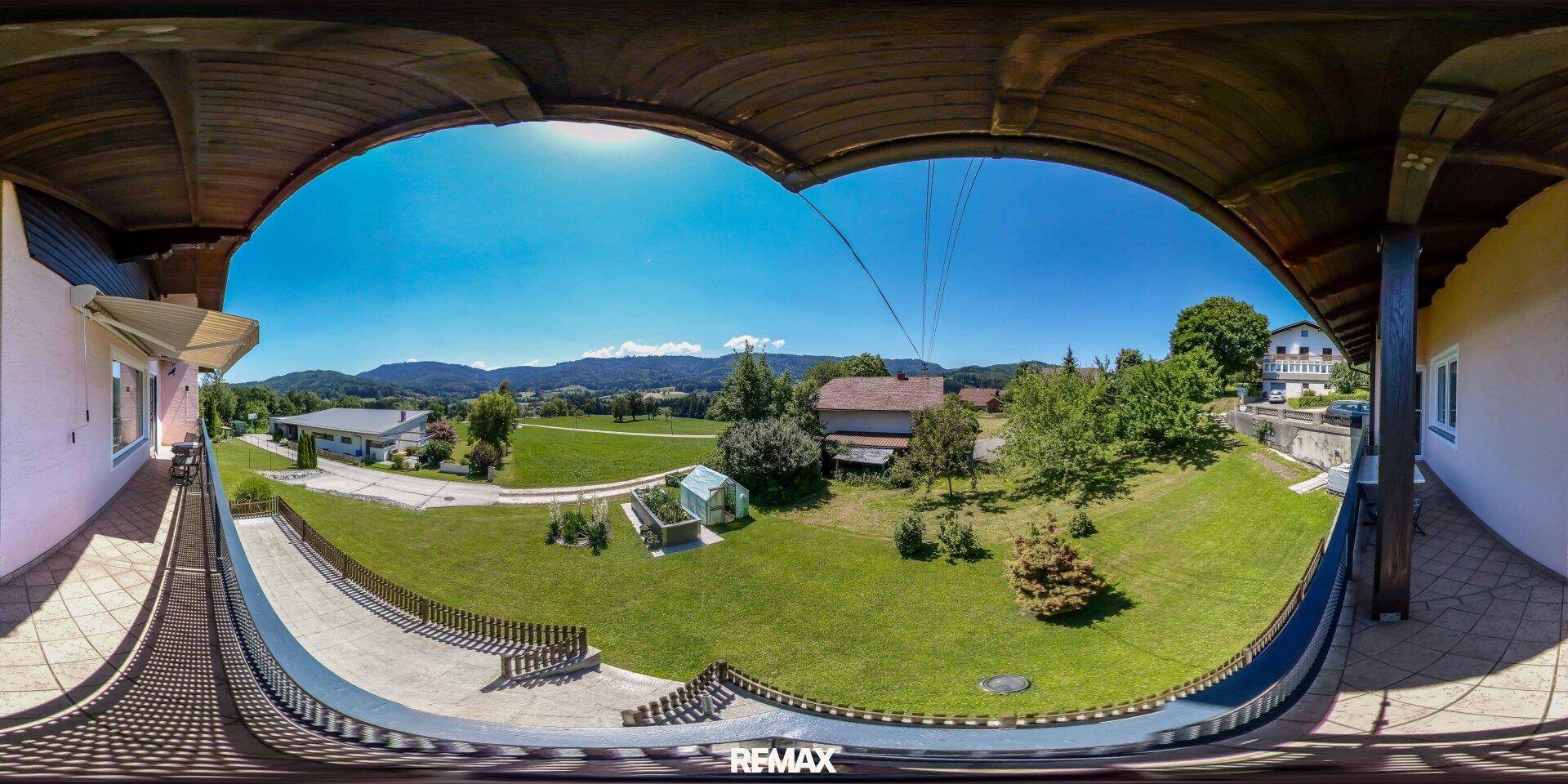 Überdachter Balkon mit Holzbalken und einem weiten, sonnigen Blick auf die umliegende Natur.