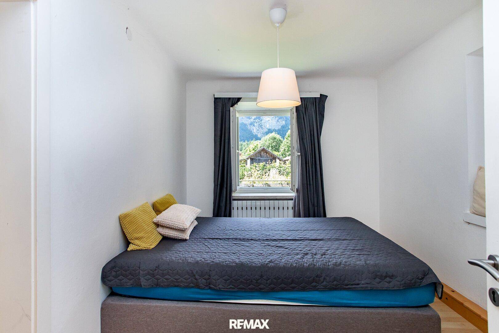 Kleines Schlafzimmer mit Doppelbett, hellem Fenster und Blick auf die umliegende Berglandschaft.