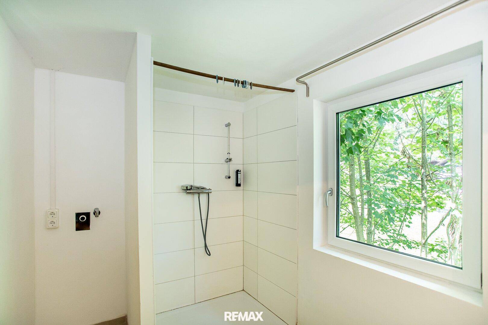 Einfaches Badezimmer mit Duschbereich und Fenster, das für gute Belüftung sorgt.