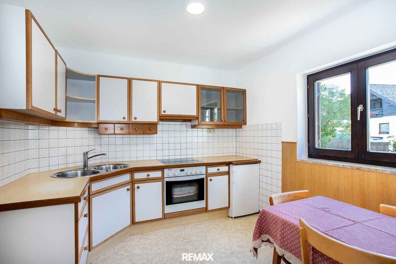 Funktionale Küche mit weißen Schränken, hellen Arbeitsplatten und Essbereich am Fenster.