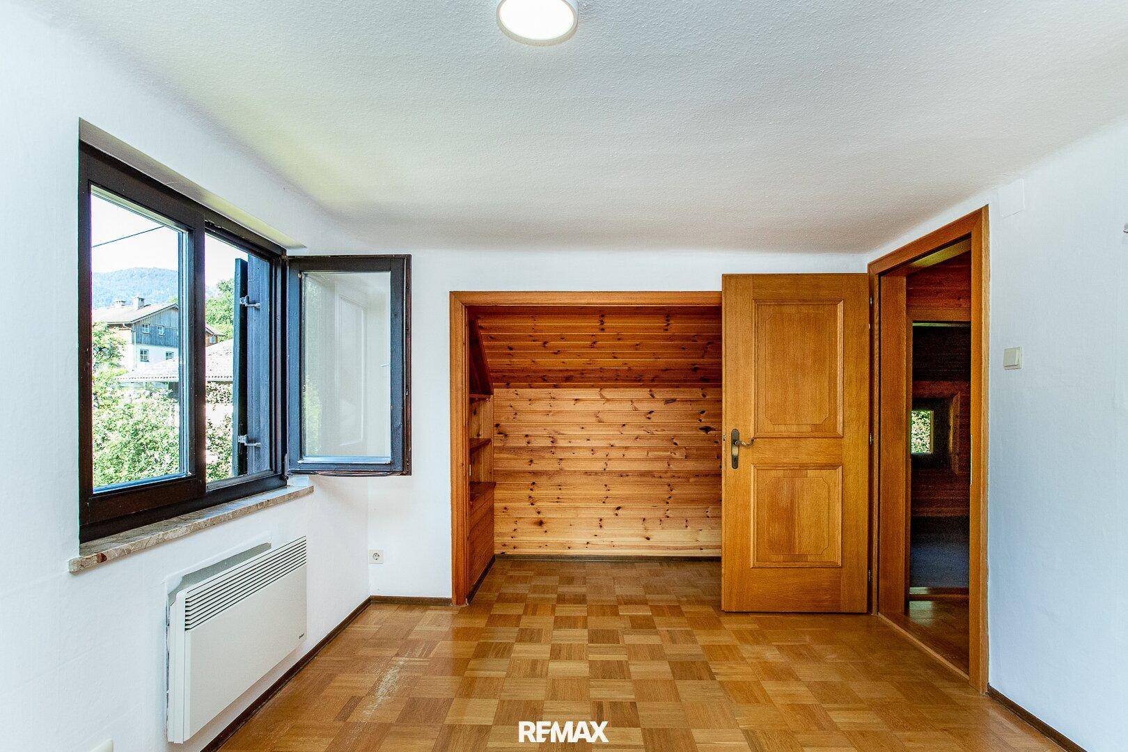 Helles Zimmer mit Parkettboden, Fenster und einer holzvertäfelten Nische, ideal als Schlafzimmer.