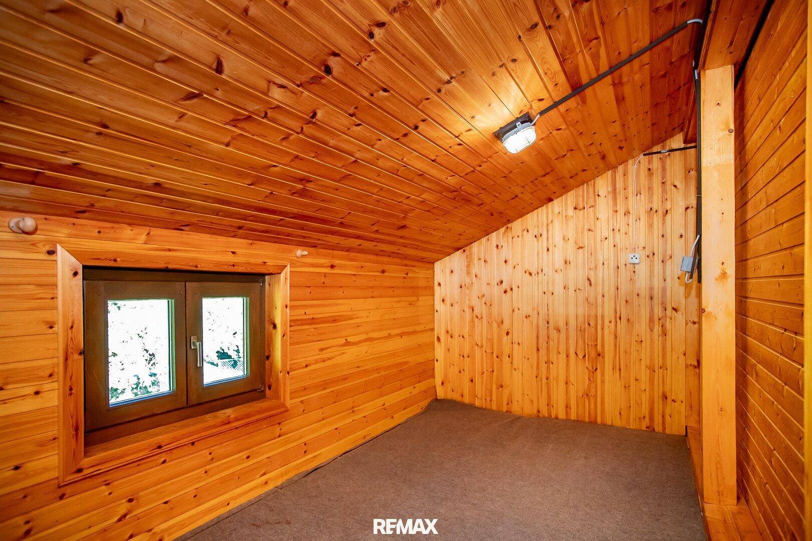 Rustikaler Dachbodenraum mit Holzvertäfelung, schräger Decke und kleinem Fenster.