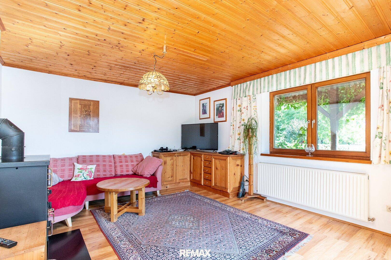 Rustikales Wohnzimmer mit Holzbalkendecke, Kaminofen und Blick ins Grüne.