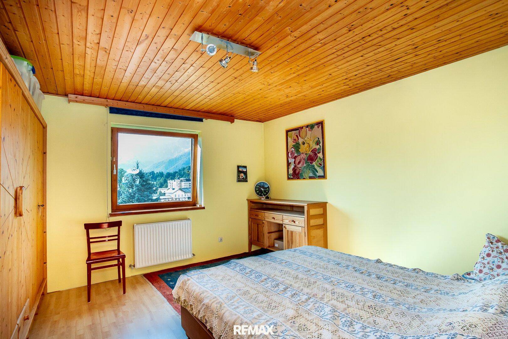 Schlafzimmer mit gelben Wänden, Holzdecke und Fenster mit Bergblick.