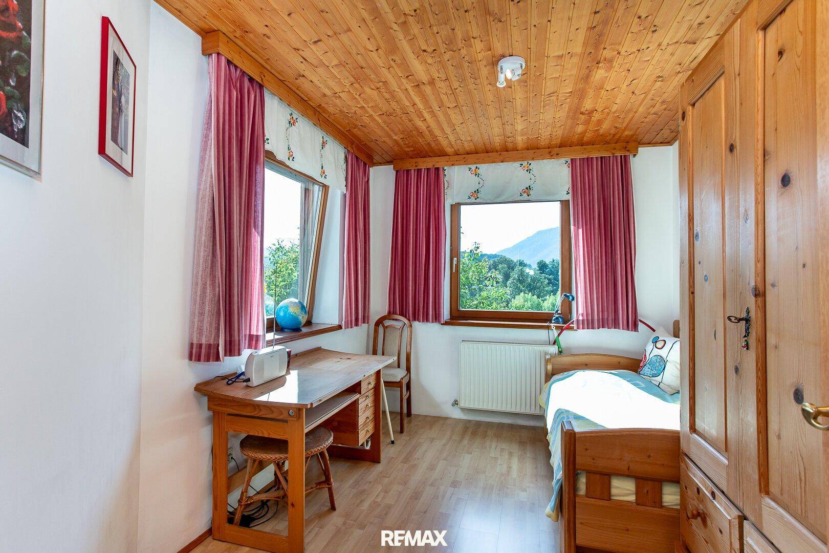 Helles Kinderzimmer mit Holzdecke, Schreibtisch und Blick ins Grüne.