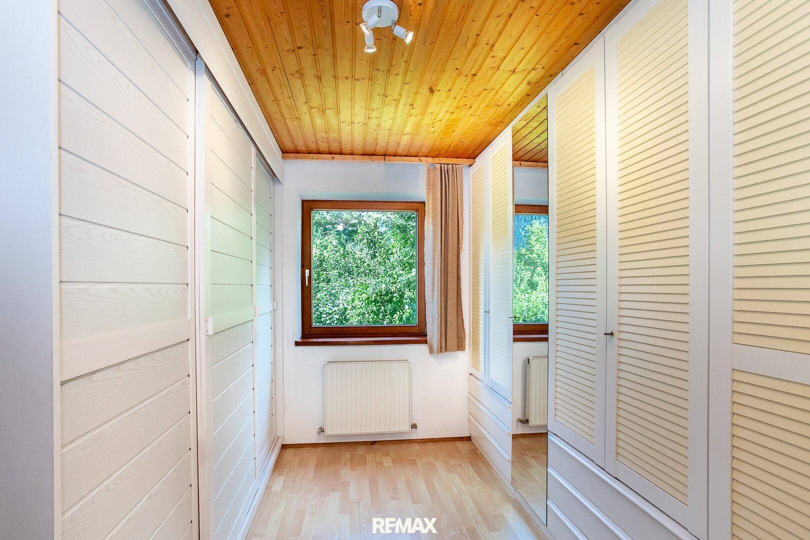 Begehbarer Kleiderschrank mit hellen Schränken, Holzdecke und Fenster.