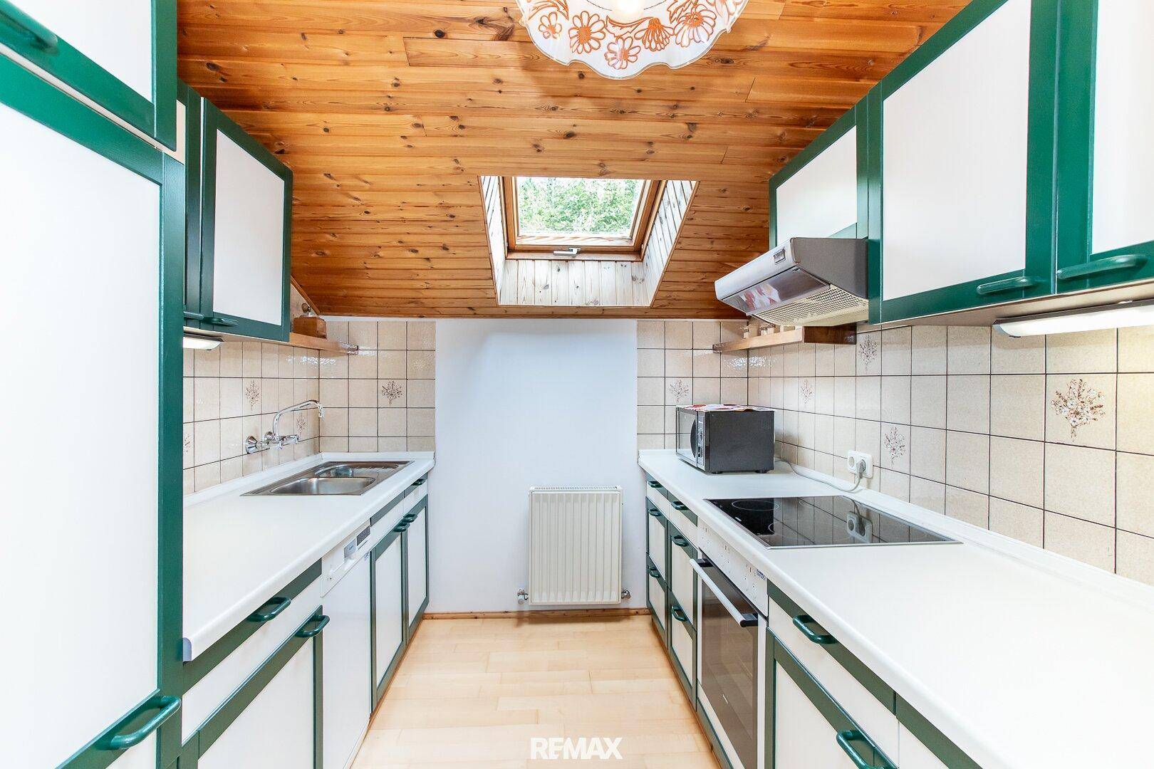 Dachgeschossküche mit grünen Schränken, Dachfenster und Holzdecke.