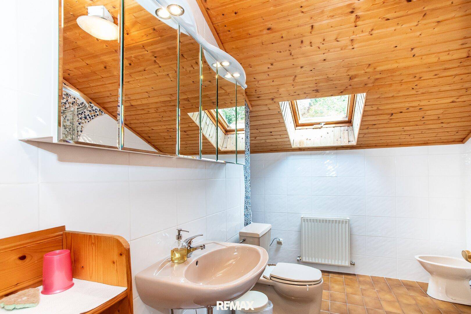 Dachgeschoss-Badezimmer mit Dachfenster, Holzdecke und Fliesenboden.