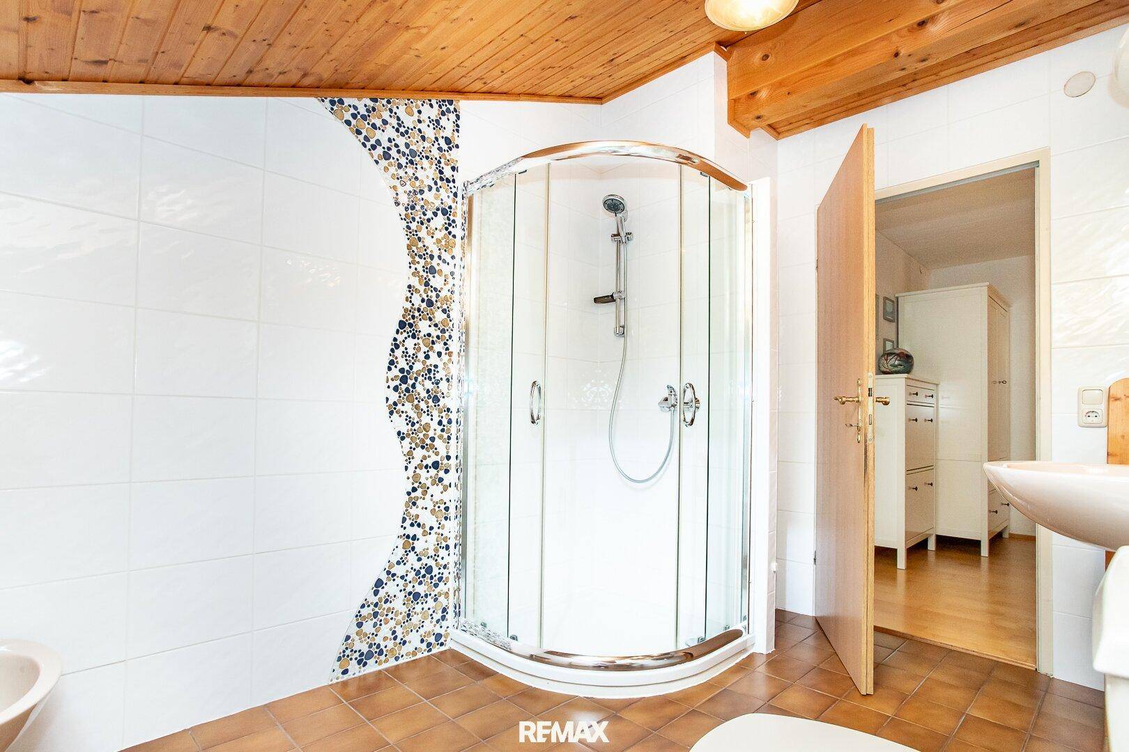 Dachgeschoss-Badezimmer mit Duschkabine, Holzdecke und Fliesenboden.