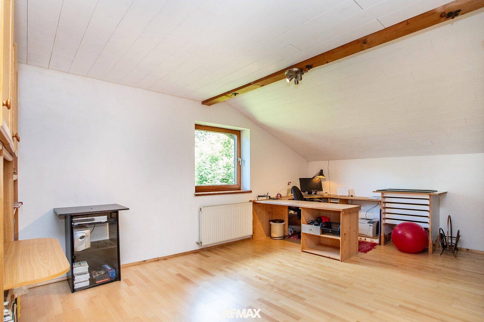 Helles Dachgeschoss-Büro mit Schreibtisch, Holzboden und Fenster.