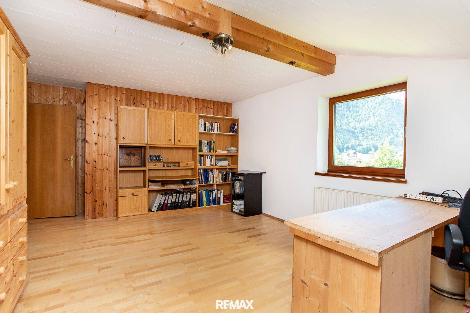 Geräumiges Dachgeschoss-Büro mit Holzvertäfelung, Bücherregal und Fenster.
