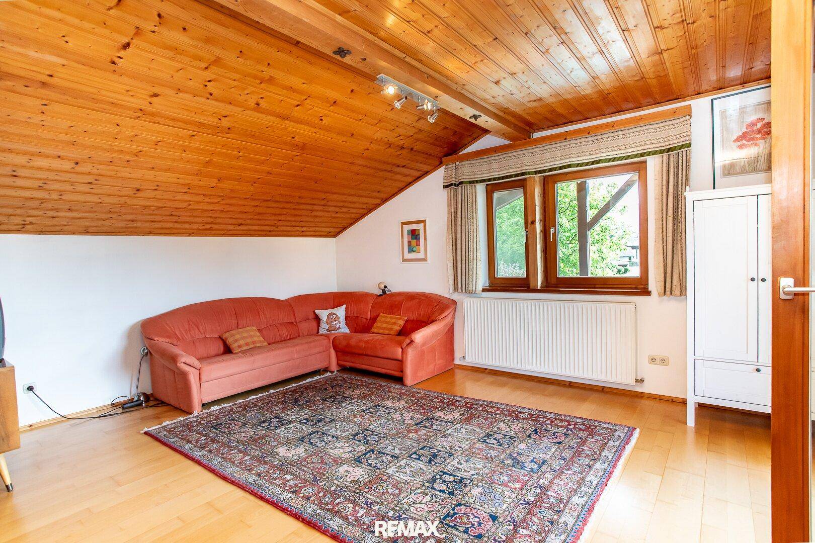 Gemütliches Dachgeschoss-Wohnzimmer mit Sofa, Teppich und Holzdecke.