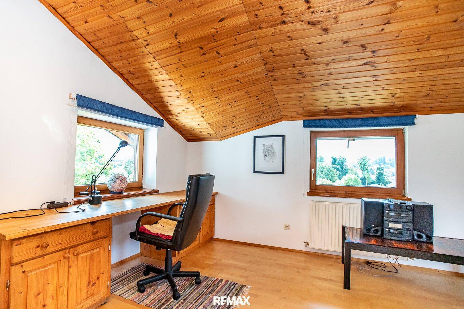 Dachgeschoss-Büro mit Holztisch, Holzdecke und Fenstern mit Ausblick.