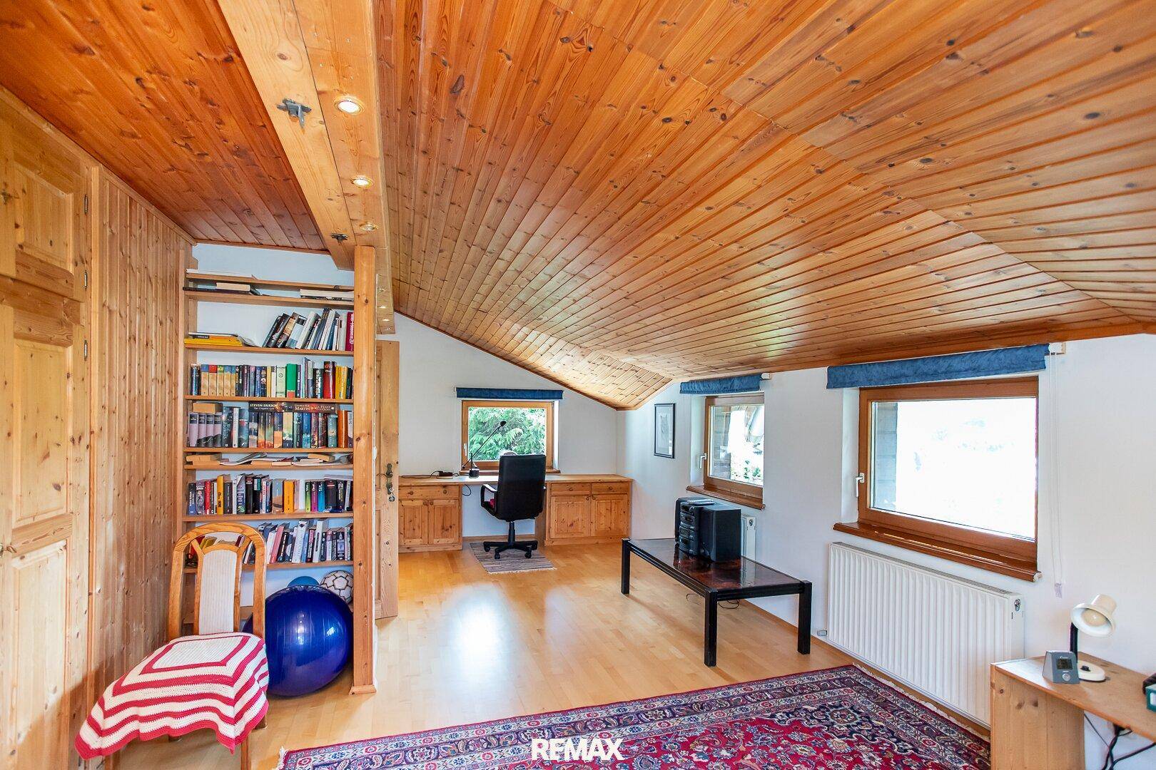 Großes Dachgeschoss-Büro mit Bücherregal, Holzboden und Fenstern.