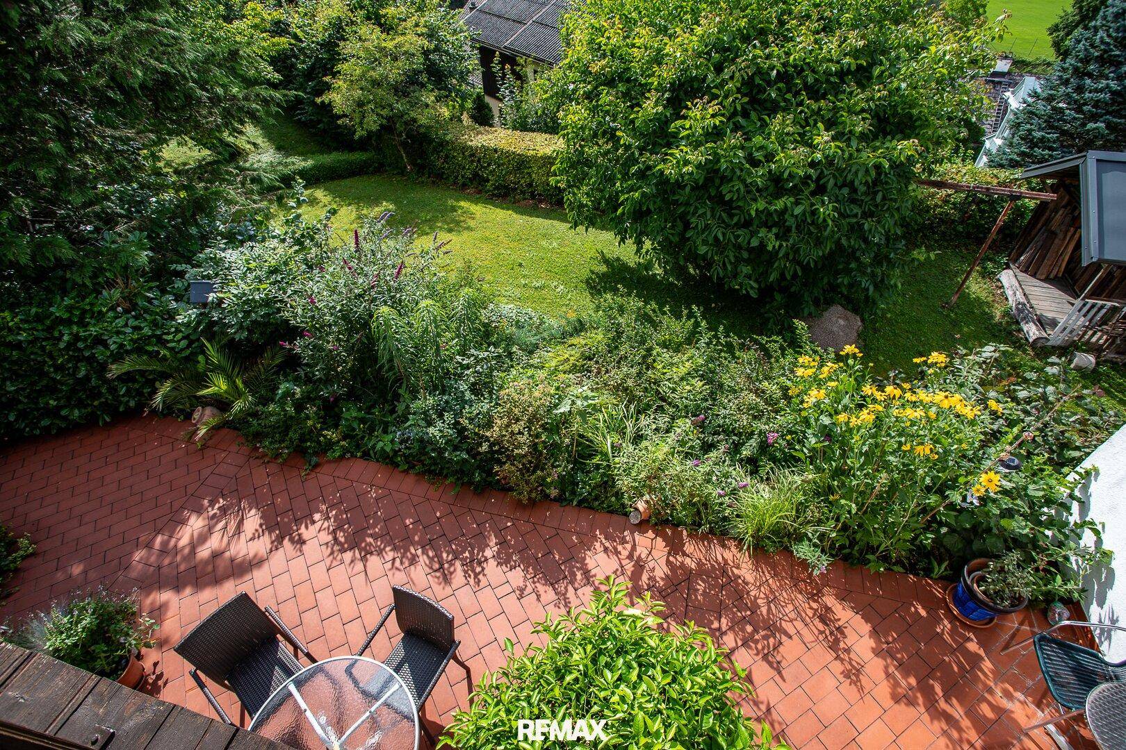 Gepflegter Gartenbereich mit Terrasse, Rasenfläche und üppiger Bepflanzung.