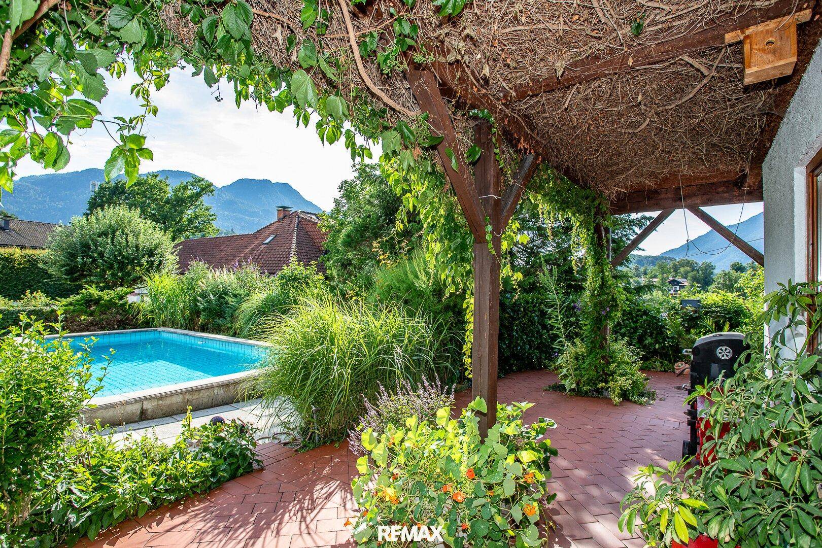 Überdachte Terrasse mit Poolzugang, üppiger Vegetation und Bergblick.