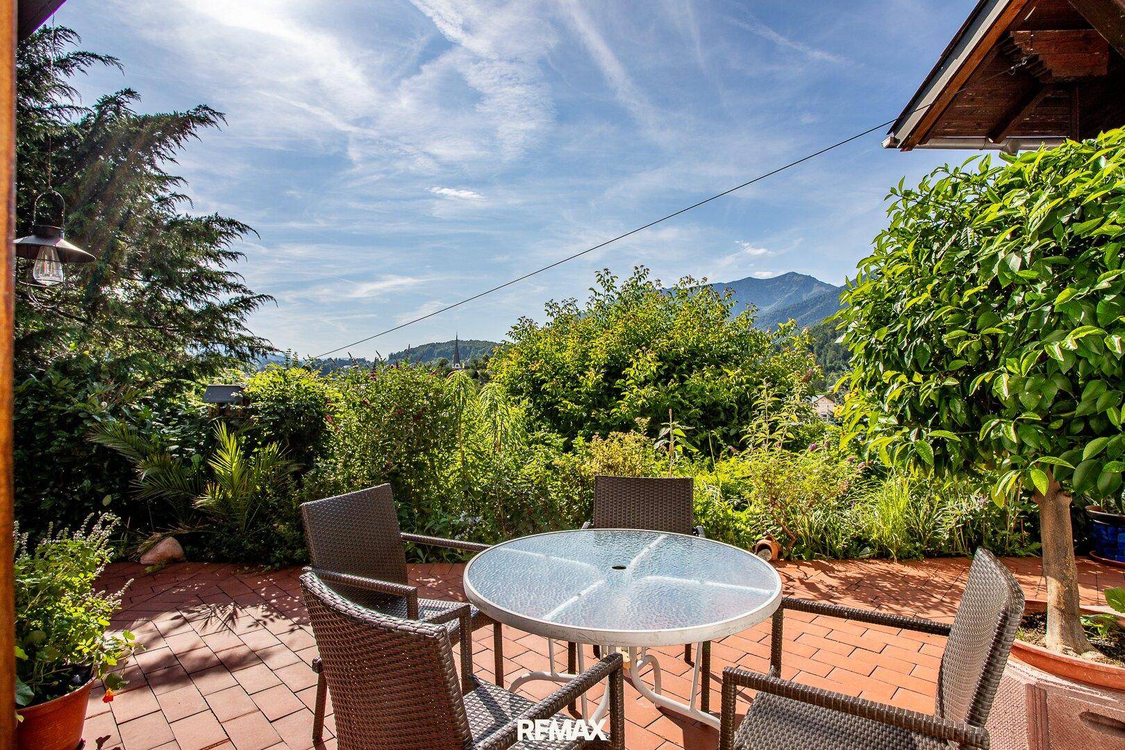 Sonniger Terrassenbereich mit Gartenmöbeln, umgeben von Grün und Bergblick.