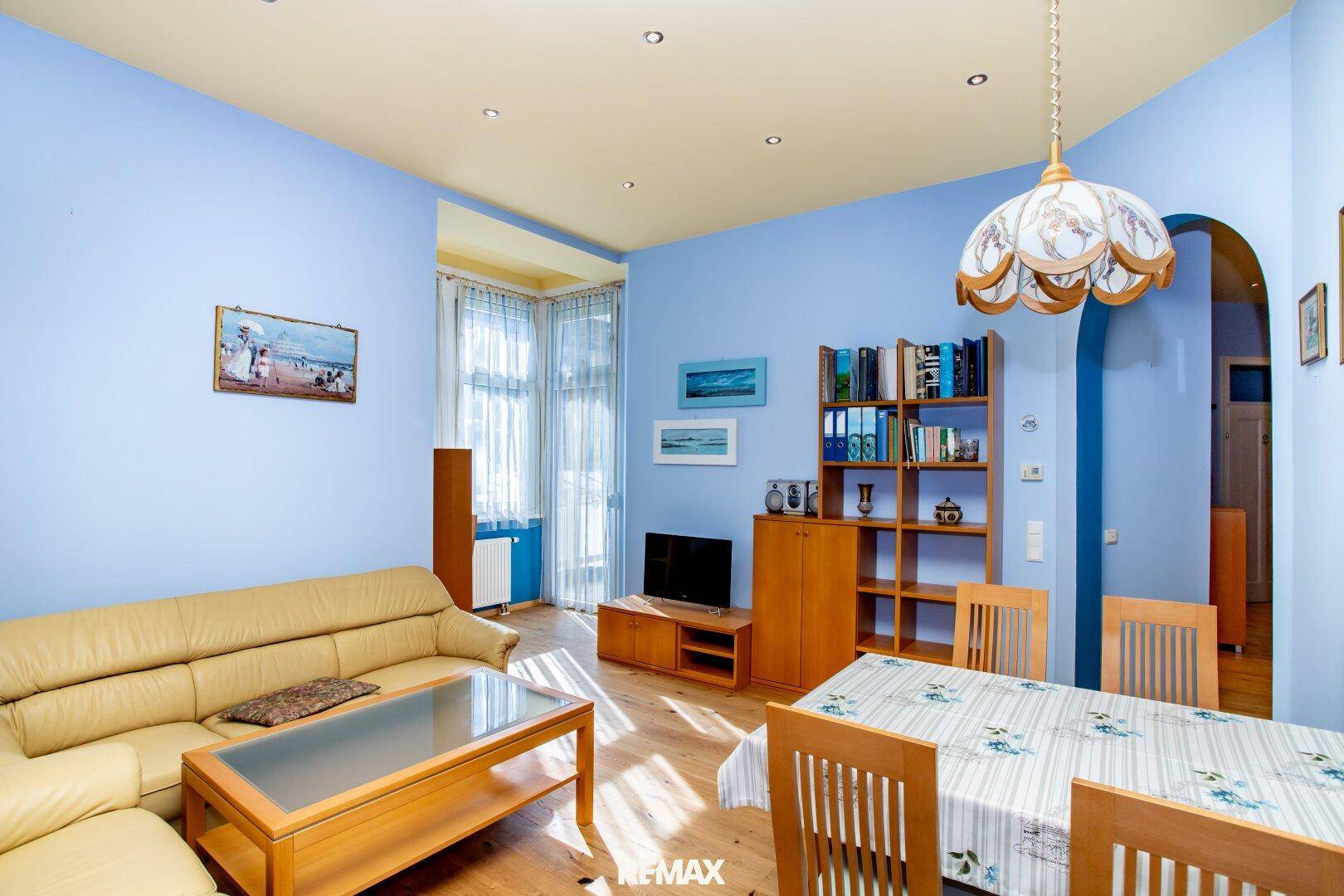 Geräumiges Wohn- und Esszimmer mit Holzboden, blauen Wänden und viel Tageslicht.