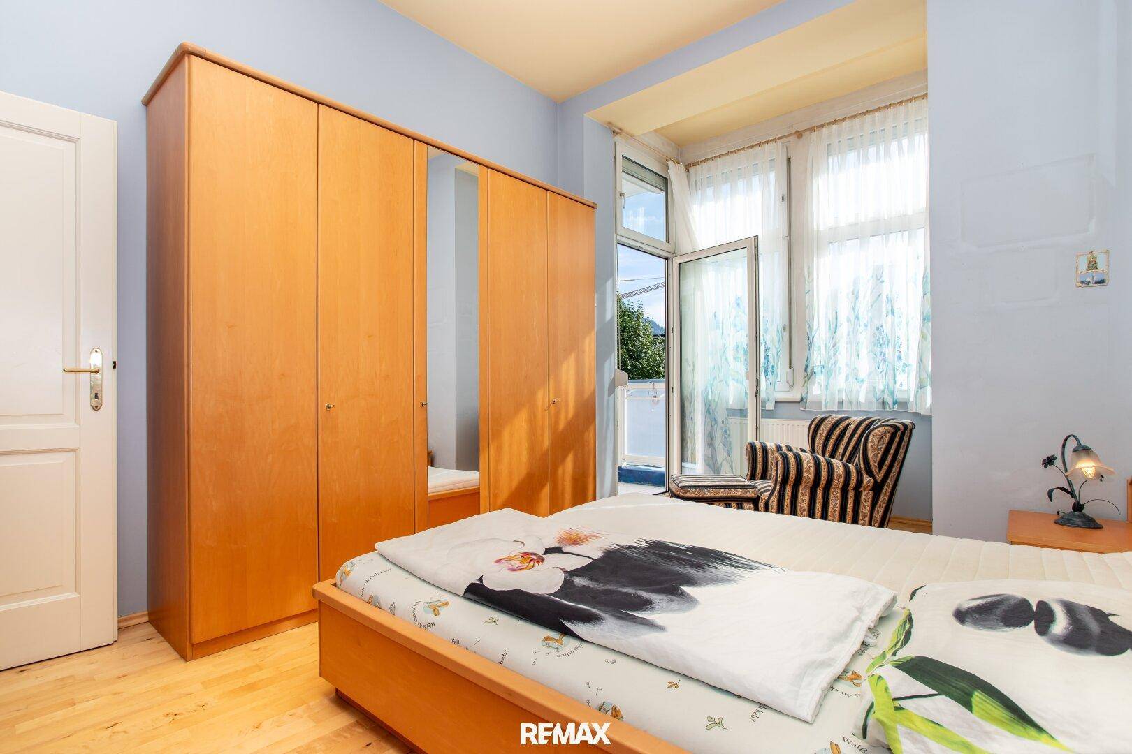 Schlafzimmer mit Holzschrank, Doppelbett und Zugang zu einem Außenbereich.
