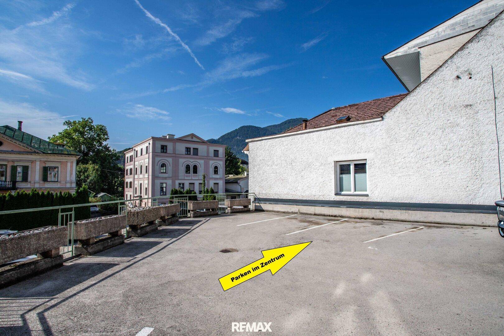 Außenparkplatz im Zentrum mit umliegenden Gebäuden und Bergen im Hintergrund.