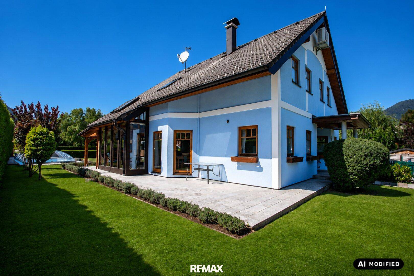 Seitenansicht des Hauses mit gepflasterter Terrasse, Rasenfläche und Blick auf die Umgebung.