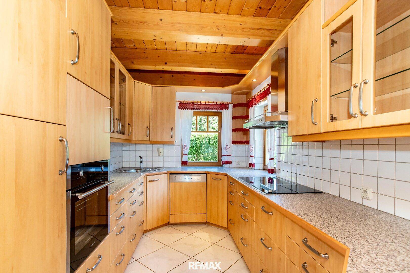 Funktionale Holzküche mit Einbaugeräten, Fliesenboden und Fenster mit Blick ins Grüne.